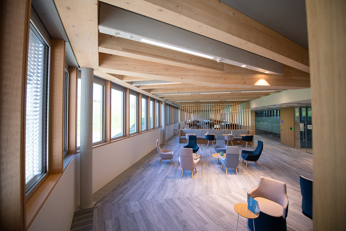 An open area with several seats and tables inside a curved room with many windows shows - The H building's interior.
